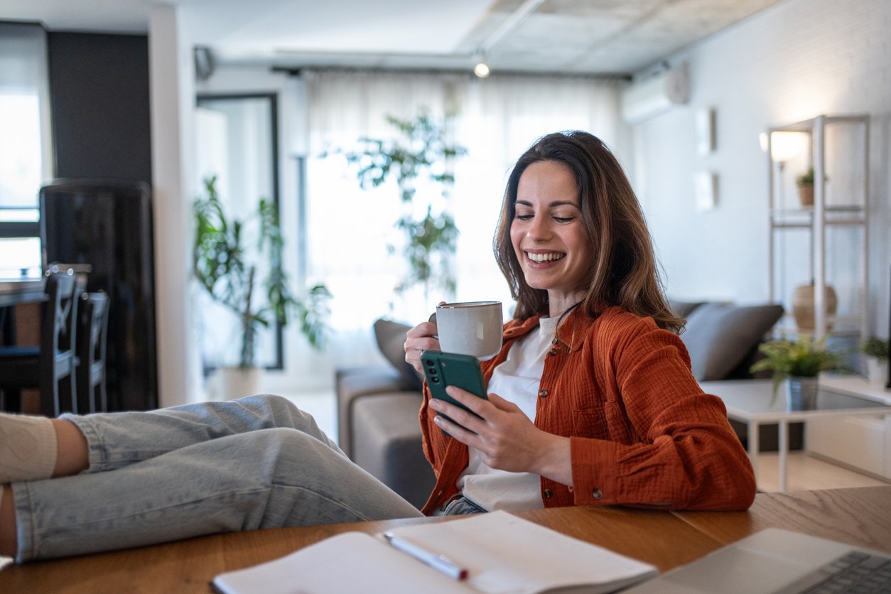 A homeowner reviewing her bids at home with a coffee, phone in hand